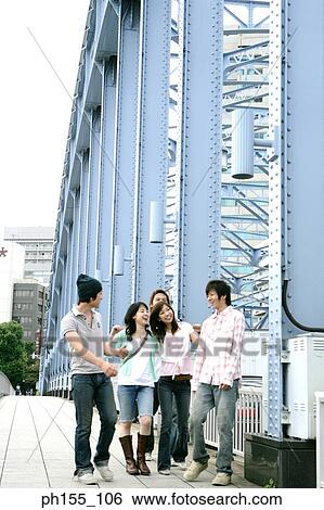 Three young men and two young women smiling and walking together on a bridge View Large Photo Image Stock Photograph - Three young men and two young women smiling and walking together on a bridge. Fotosearch
