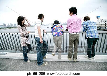 Three young men and two young women leaning against a railing View Large Photo Image Stock Photograph - Three young men and two young women leaning against a railing. Fotosearch