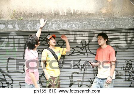 Three young men standing together in front of a wall View Large Photo Image Stock Image - Three young men standing together in front of a wall. Fotosearch