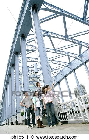 Stock Image - Three young men with two young women standing on a bridge and looking up. Fotosearch