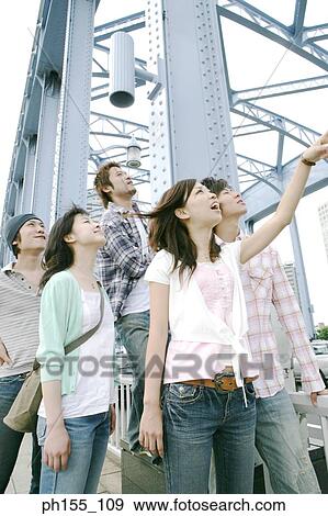 Stock Photo - Three young men with two young women standing on a bridge and looking up. Fotosearch