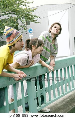 Two young men and a young woman leaning over a railing View Large Photo Image Stock Image - Two young men and a young woman leaning over a railing. Fotosearch