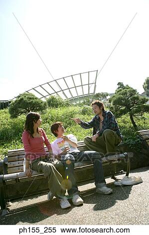 Two young men and a young woman sitting on a park bench and smiling View Large Photo Image Stock Photography - Two young men and a young woman sitting on a park bench and smiling. Fotosearch