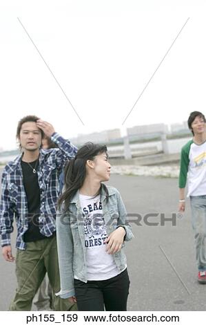 Stock Photo - Two young men and a young woman walking on the road. Fotosearch