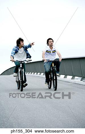 Two young men riding bicycles and pointing forward View Large Photo Image Picture - Two young men riding bicycles and pointing forward. Fotosearch