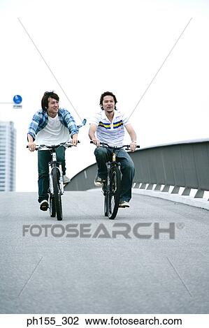 Two young men riding bicycles View Large Photo Image Stock Image - Two young men riding bicycles. Fotosearch