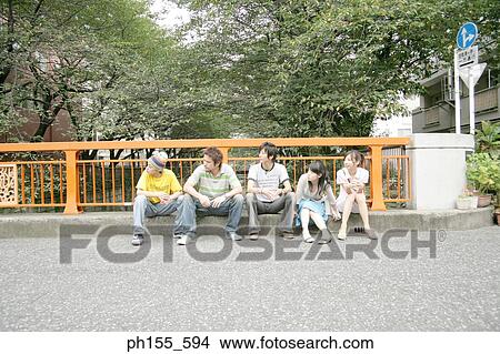 Picture - Two young women and three young men sitting in front of a railing and looking sideways. Fotosearch