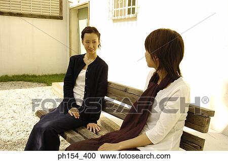 Two young women sitting on a bench and looking at each other View Large Photo Image Stock Image - Two young women sitting on a bench and looking at each other. Fotosearch