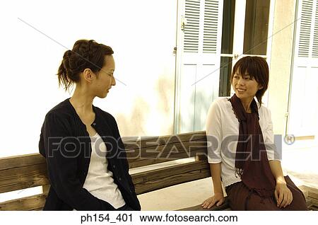 Two young women sitting on a bench and looking at each other View Large Photo Image Stock Image - Two young women sitting on a bench and looking at each other. Fotosearch