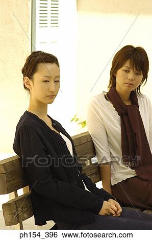 Stock Photograph - Two young women sitting together on a bench. Fotosearch