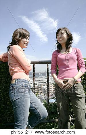 Two young women standing by a railing and smiling View Large Photo Image Stock Photo - Two young women standing by a railing and smiling. Fotosearch
