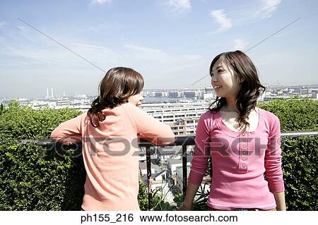 Two young women standing by a railing and smiling View Large Photo Image Stock Photograph - Two young women standing by a railing and smiling. Fotosearch