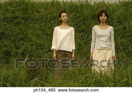Two young women standing in a field View Large Photo Image Stock Image - Two young women standing in a field. Fotosearch