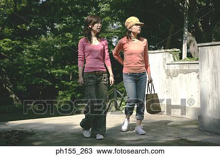 Two young women walking in a park View Large Photo Image Stock Image - Two young women walking in a park. Fotosearch
