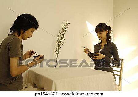 Stock Image - Young couple holding bowls and chopsticks. Fotosearch