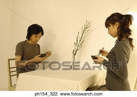 Stock Image - Young couple holding bowls and chopsticks. Fotosearch