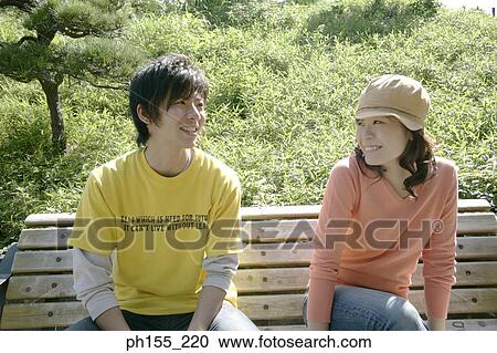 Young couple sitting on a park bench and smiling View Large Photo Image Stock Image - Young couple sitting on a park bench and smiling. Fotosearch