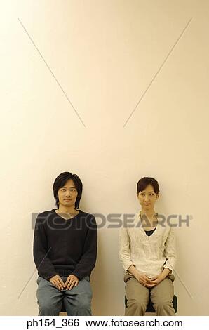 Stock Photograph - Young couple sitting on stools and looking away. Fotosearch
