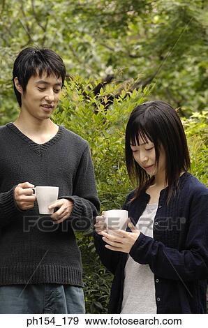 Stock Photo - Young couple standing together holding coffee cups. Fotosearch
