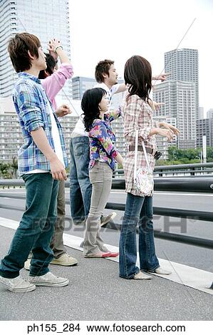 Picture - Young man and a young woman pointing forward with two young men and a young woman beside them. Fotosearch