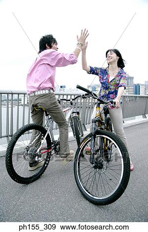Young man and a young woman sitting on a bicycle and giving high-five View Large Photo Image Stock Photo - Young man and a young woman sitting on a bicycle and giving high-five. Fotosearch