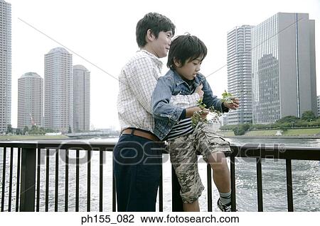 Young man and his son sitting on a railing View Large Photo Image Stock Image - Young man and his son sitting on a railing. Fotosearch