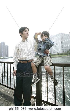 Young man and his son sitting on a railing View Large Photo Image Stock Photograph - Young man and his son sitting on a railing. Fotosearch