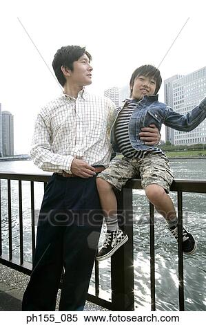 Young man and his son sitting on a railing View Large Photo Image Stock Photography - Young man and his son sitting on a railing. Fotosearch