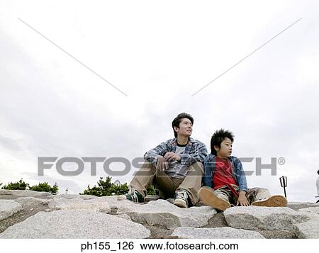 Young man and his son sitting together and looking away View Large Photo Image Stock Photograph - Young man and his son sitting together and looking away. Fotosearch