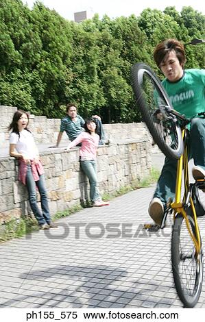 Stock Photography - Young man doing a wheelie on a bicycle. Fotosearch