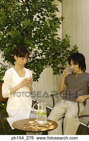 Stock Photo - Young man drinking a glass of water with a young woman sitting beside him. Fotosearch