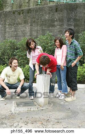 Young man drinking water from a drinking fountain with his friend standing beside him View Large Photo Image Stock Photograph - Young man drinking water from a drinking fountain with his friend standing beside him. Fotosearch