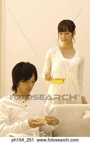 Young man holding a cup of tea with a young woman holding a teapot behind him View Large Photo Image Stock Image - Young man holding a cup of tea with a young woman holding a teapot behind him. Fotosearch