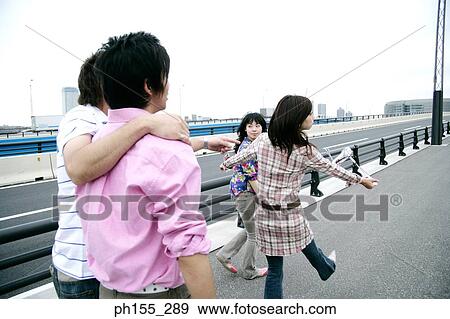Stock Photo - Young man pointing at two young women walking on the road. Fotosearch