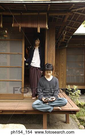 Young man reading a book with a young woman standing at the door View Large Photo Image Picture - Young man reading a book with a young woman standing at the door. Fotosearch