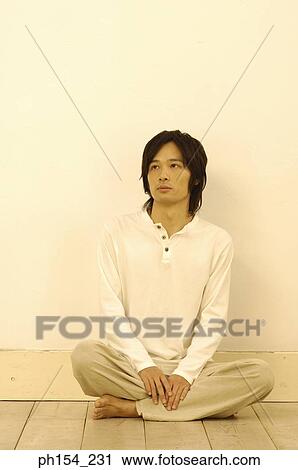 Stock Image - Young man sitting on the floor with his legs crossed. Fotosearch