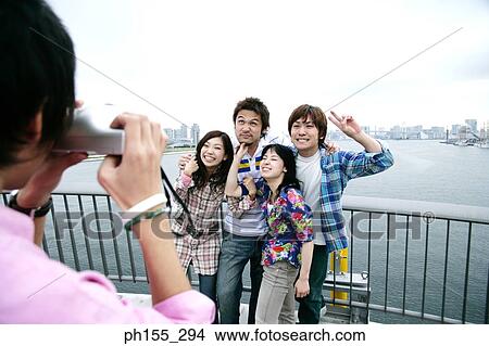 Picture - Young man taking a picture of four people. Fotosearch