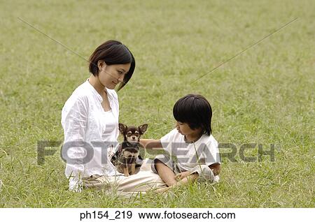 Stock Photo - Young woman and her daughter sitting on the grass with their dog. Fotosearch