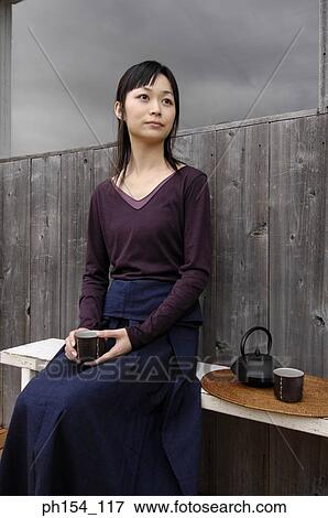 Young woman holding a cup and sitting on a bench View Large Photo Image Stock Photo - Young woman holding a cup and sitting on a bench. Fotosearch