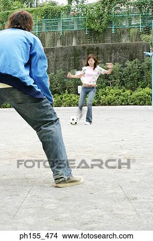 Picture - Young woman kicking a football with a young man in front of her. Fotosearch
