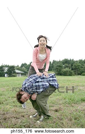 Stock Photograph - Young woman leapfrogging over a young man. Fotosearch