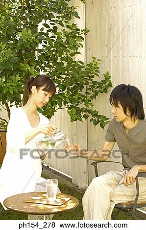 Young woman pouring water into a glass held by a young man View Large Photo Image Stock Photo - Young woman pouring water into a glass held by a young man. Fotosearch