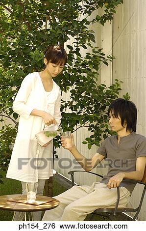 Stock Photograph - Young woman pouring water into a glass held by a young man. Fotosearch