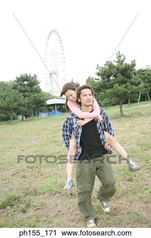 Stock Image - Young woman riding piggyback on a young man. Fotosearch