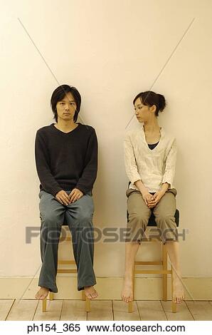 Stock Photography - Young woman sitting on a stool and looking at a young man sitting beside her. Fotosearch