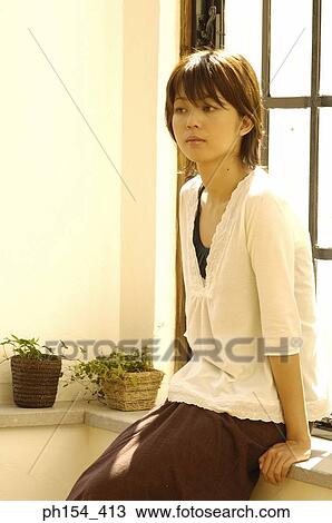 Young woman sitting on a window sill and looking away View Large Photo Image Stock Image - Young woman sitting on a window sill and looking away. Fotosearch