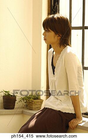 Young woman sitting on a window sill and looking away View Large Photo Image Stock Photography - Young woman sitting on a window sill and looking away. Fotosearch