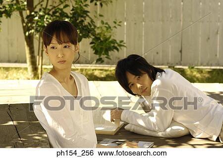 Stock Photograph - Young woman sitting with a young man lying beside her. Fotosearch