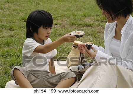 Young woman sitting with her daughter on a mat and eating food View Large Photo Image Stock Photo - Young woman sitting with her daughter on a mat and eating food. Fotosearch