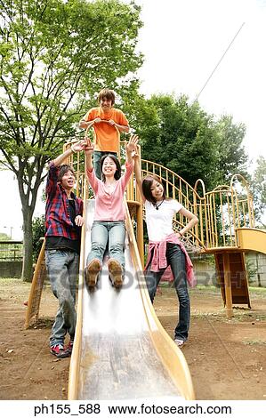 Stock Photo - Young woman sliding on a slide with her friends standing beside her. Fotosearch